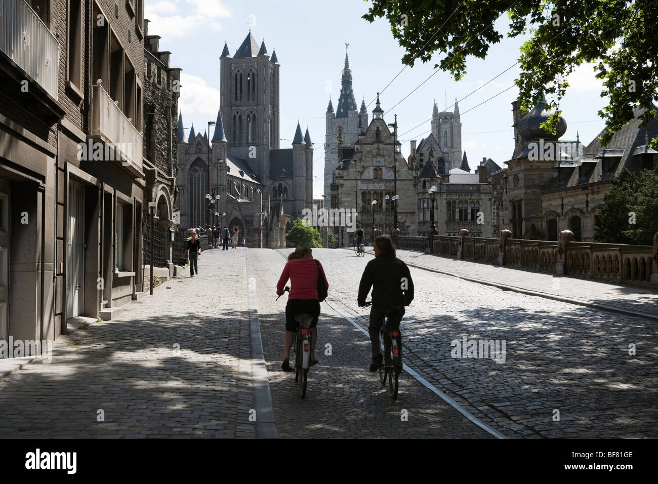 Cyclists crossing Saint Michael`s Bridge with Saint Niklaaskerk and the Belfry behind. Stock Photo